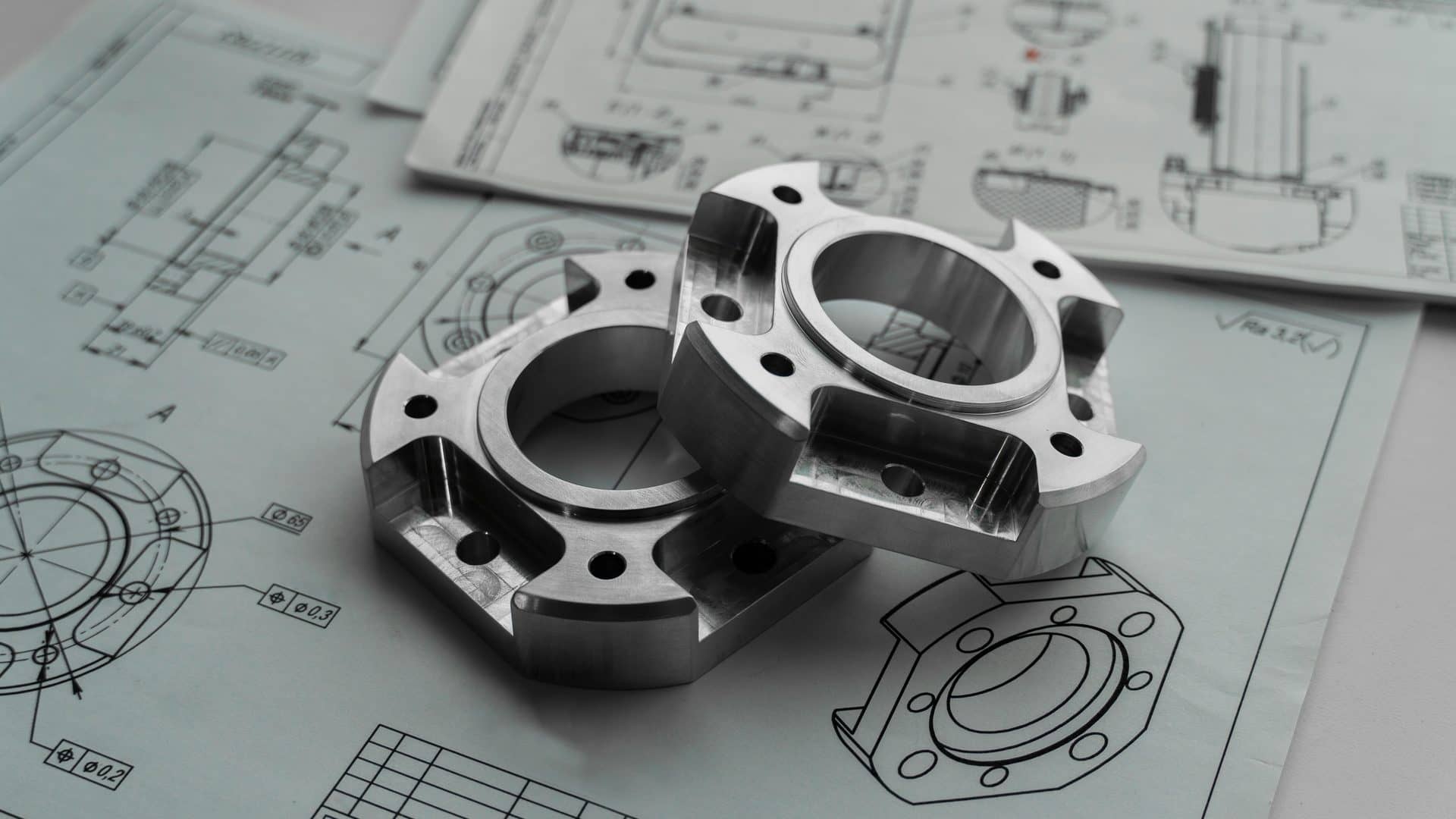 CNC machined metal flanges resting on engineering drawings