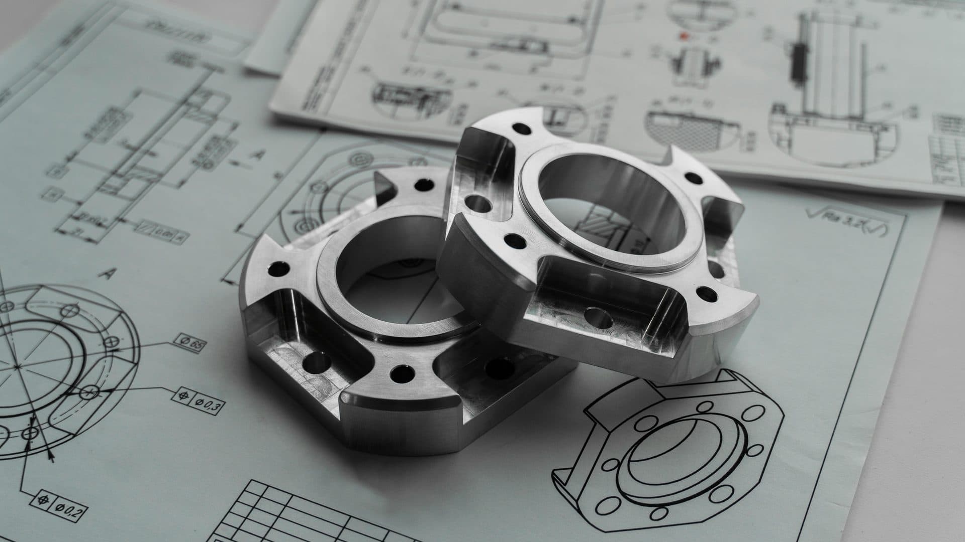 CNC machined metal flanges resting on engineering drawings